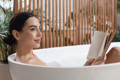 Photo of Beautiful young woman reading book while taking bath at home