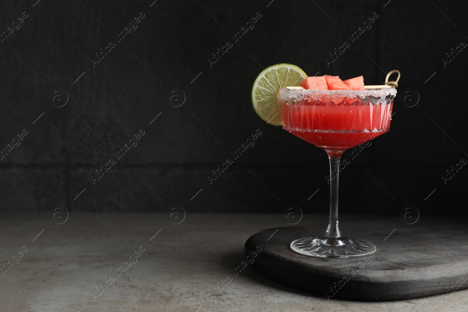 Photo of Cocktail glass of delicious fresh watermelon juice with lime on grey table. Space for text