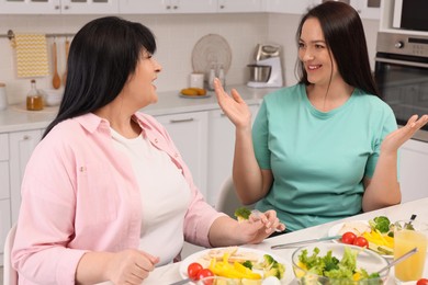 Photo of Happy overweight women having healthy meal together at table in kitchen