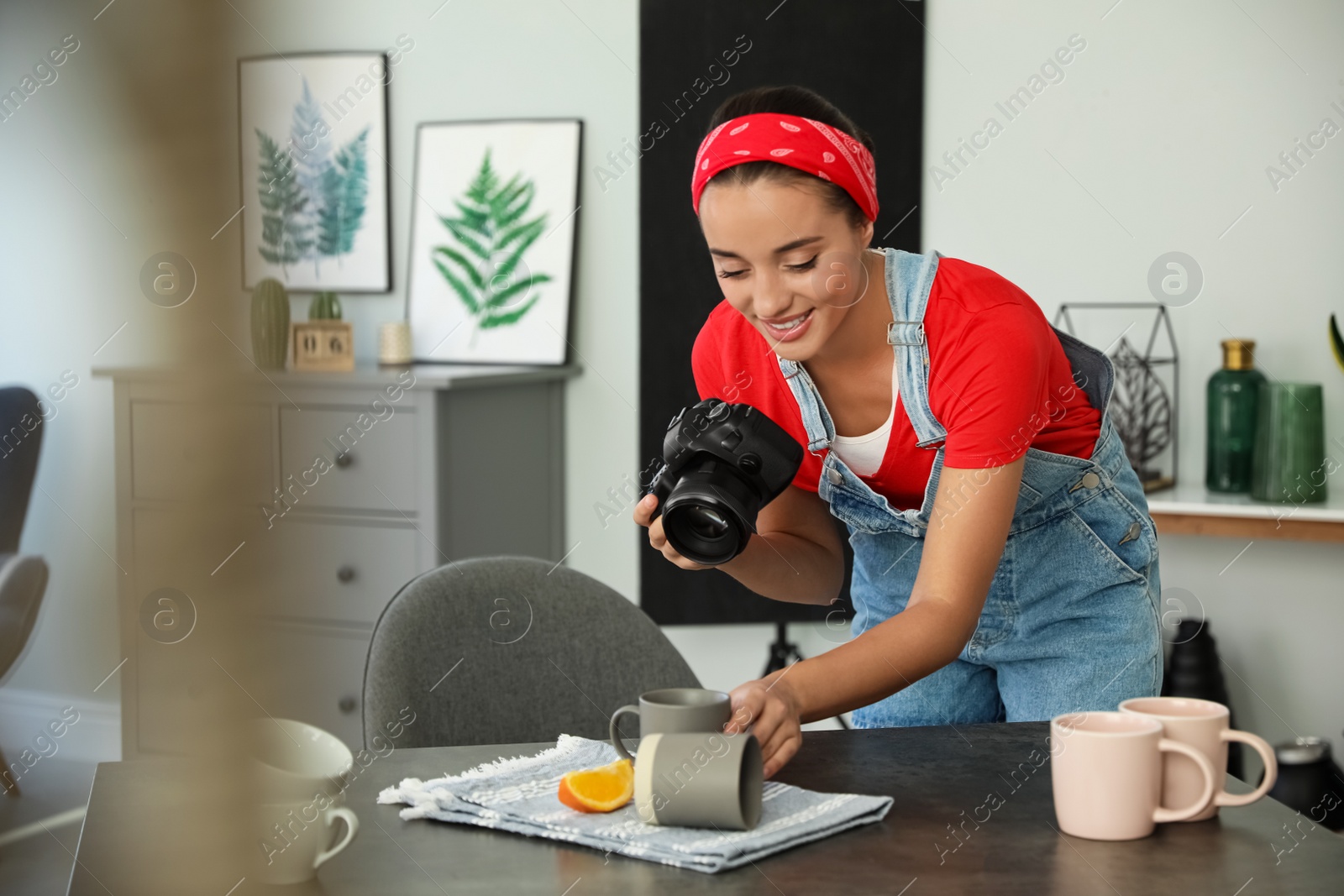 Photo of Young photographer taking picture of cups at table indoors