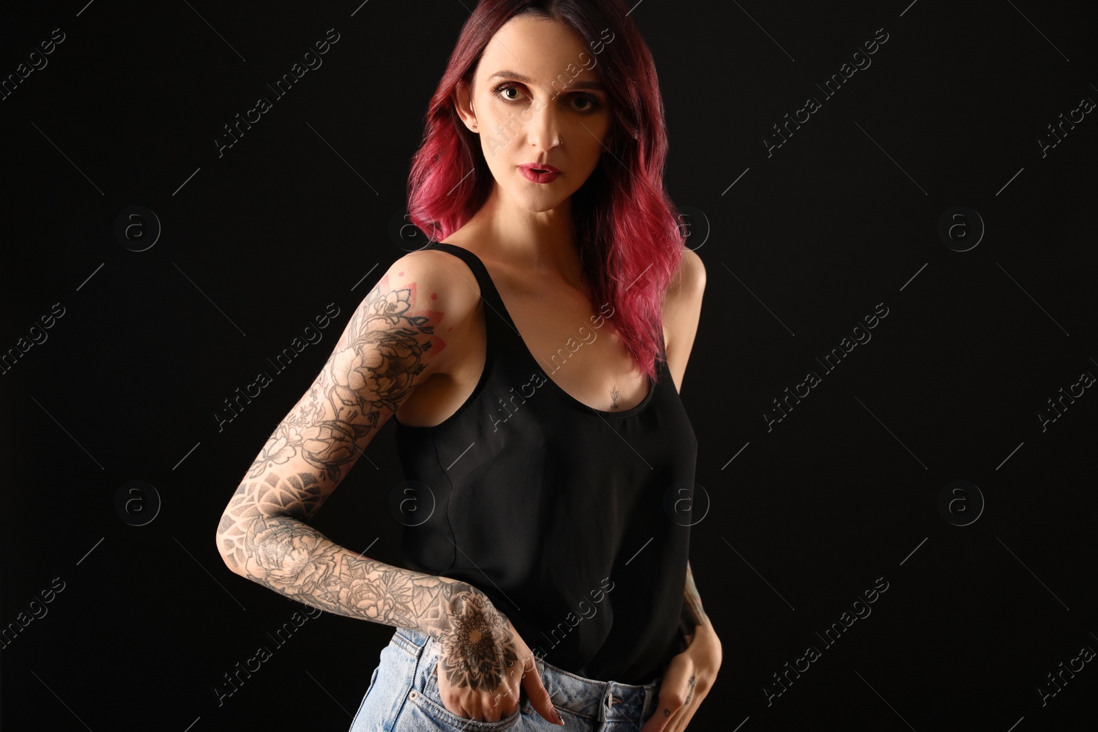 Photo of Beautiful woman with tattoos on arms against black background