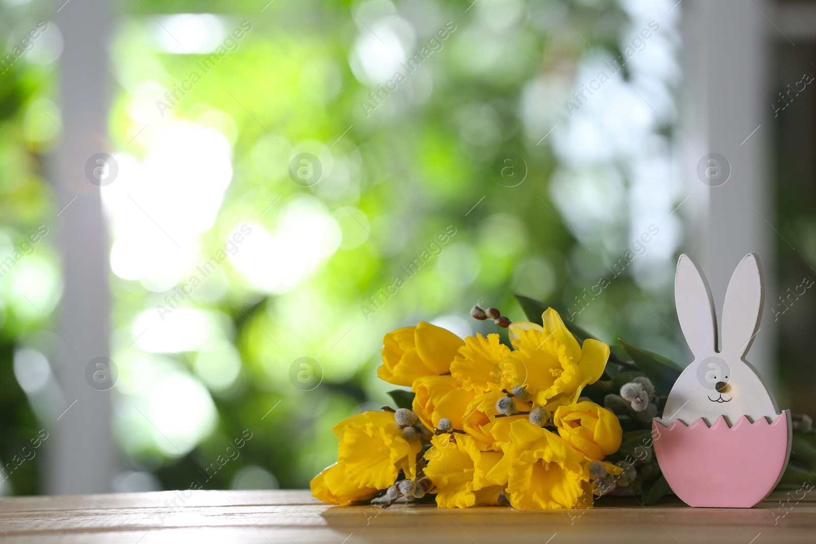 Photo of Easter bunny figure and flowers on wooden table against blurred green background. Space for text