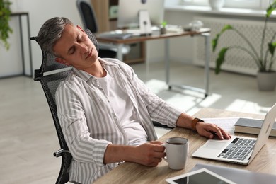 Photo of Man with cup of drink snoozing at wooden table in office