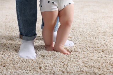 Photo of Mother supporting her baby son while he learning to walk on carpet, closeup. Space for text