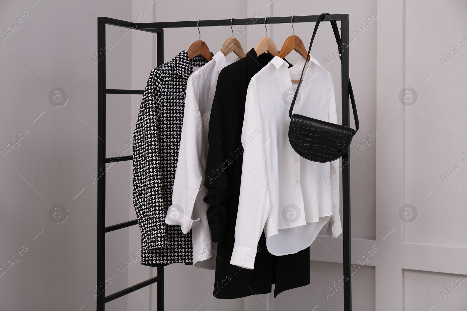 Photo of Rack with stylish women's clothes and bag near light wall