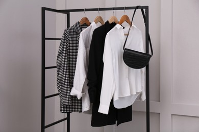 Photo of Rack with stylish women's clothes and bag near light wall