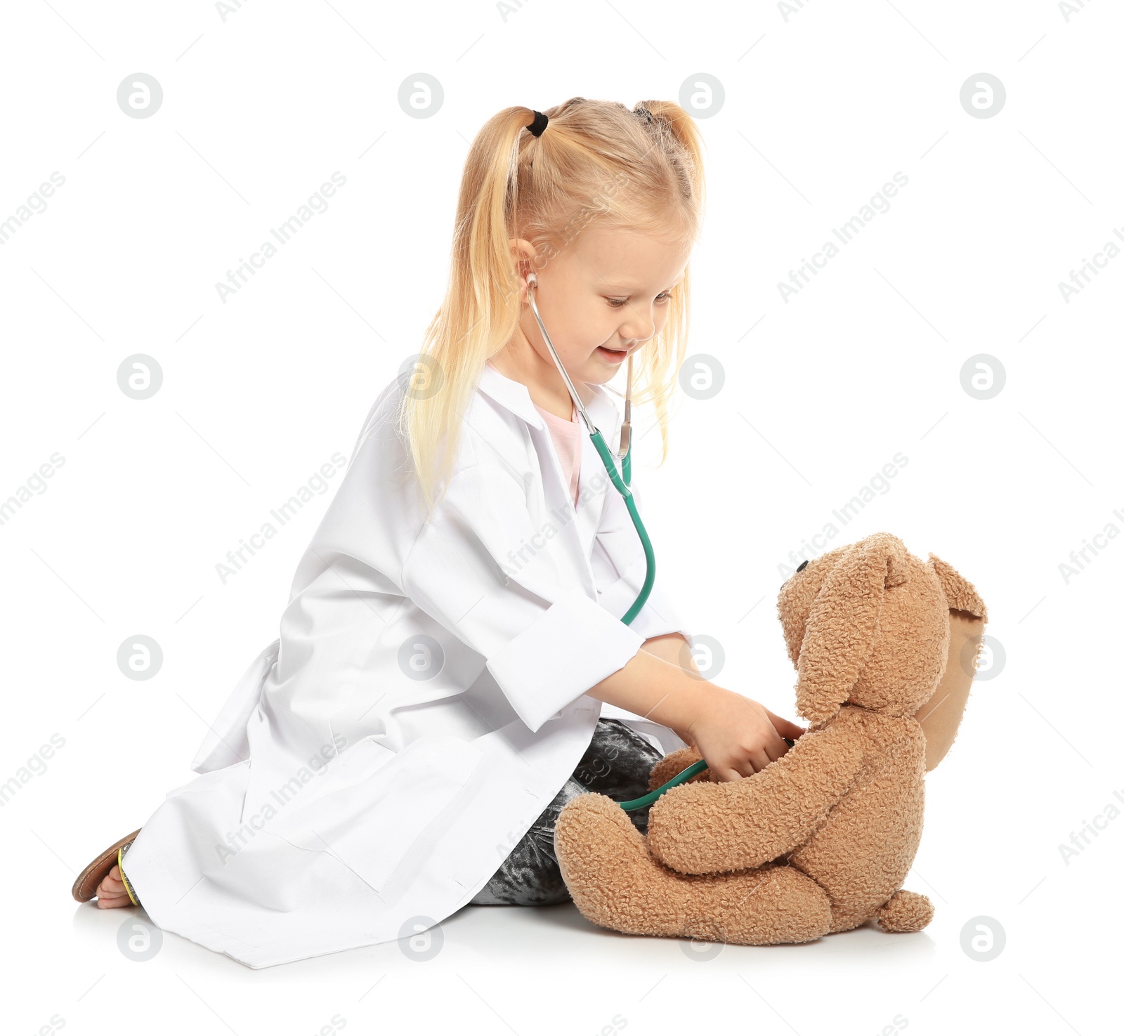 Photo of Cute child imagining herself as doctor while playing with stethoscope and toy bunny on white background