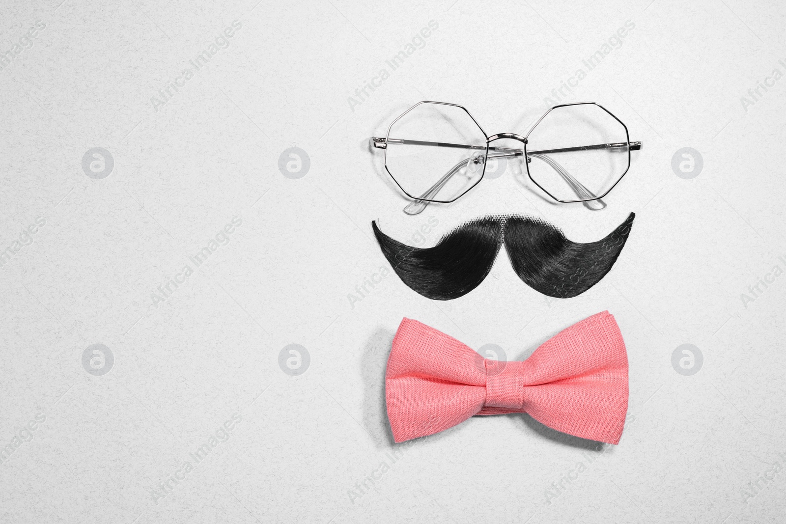 Photo of Man's face made of artificial mustache, bow tie and glasses on light grey background, top view. Space for text