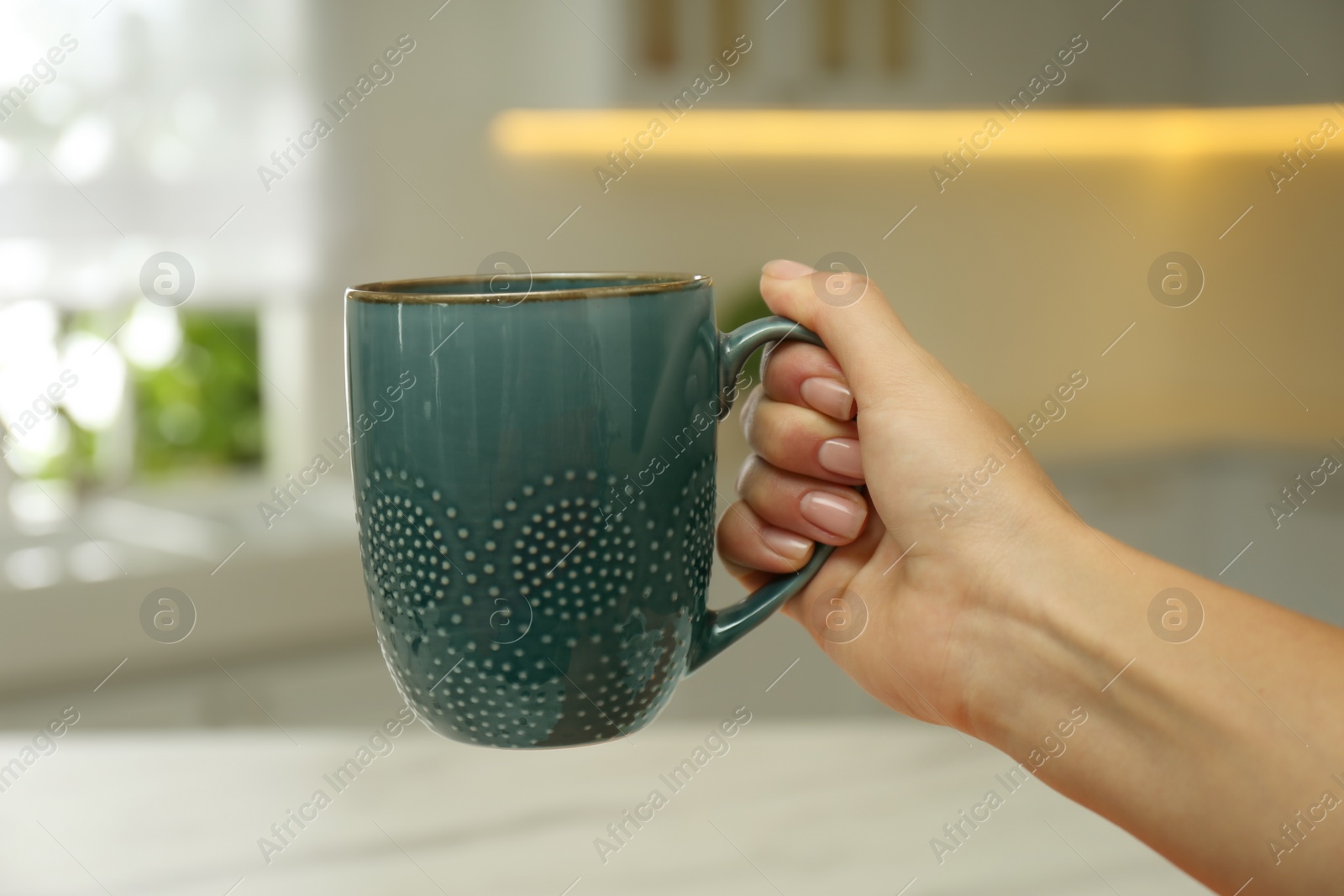 Photo of Woman holding elegant blue cup in kitchen, closeup
