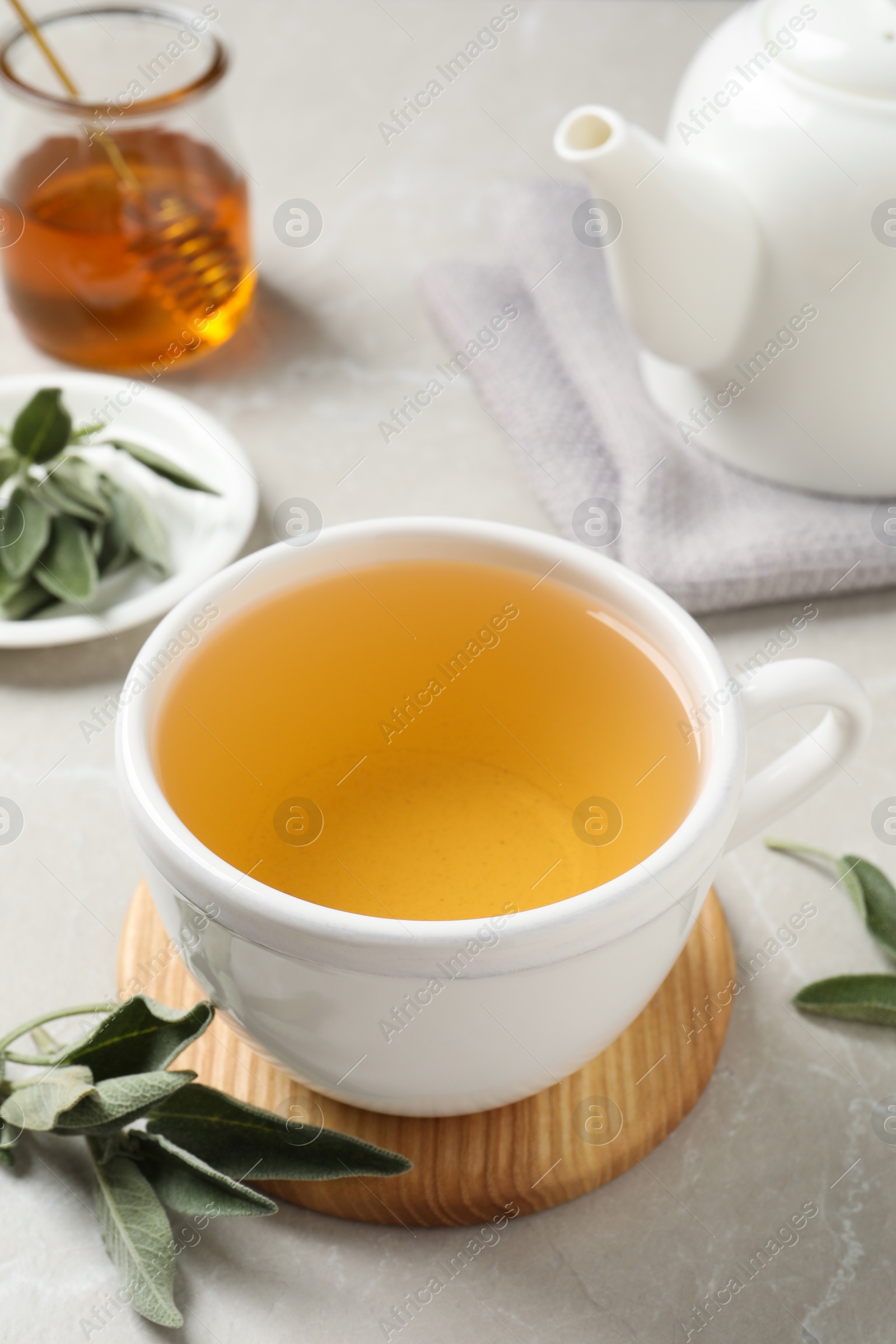 Photo of Cup of aromatic sage tea and fresh leaves on light grey table