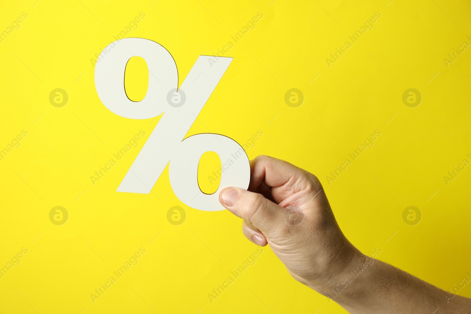 Photo of Man holding percent sign on yellow background, closeup