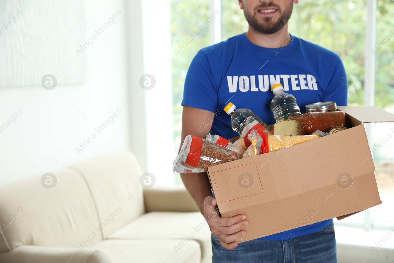 Photo of Male volunteer holding box with donations indoors. Space for text