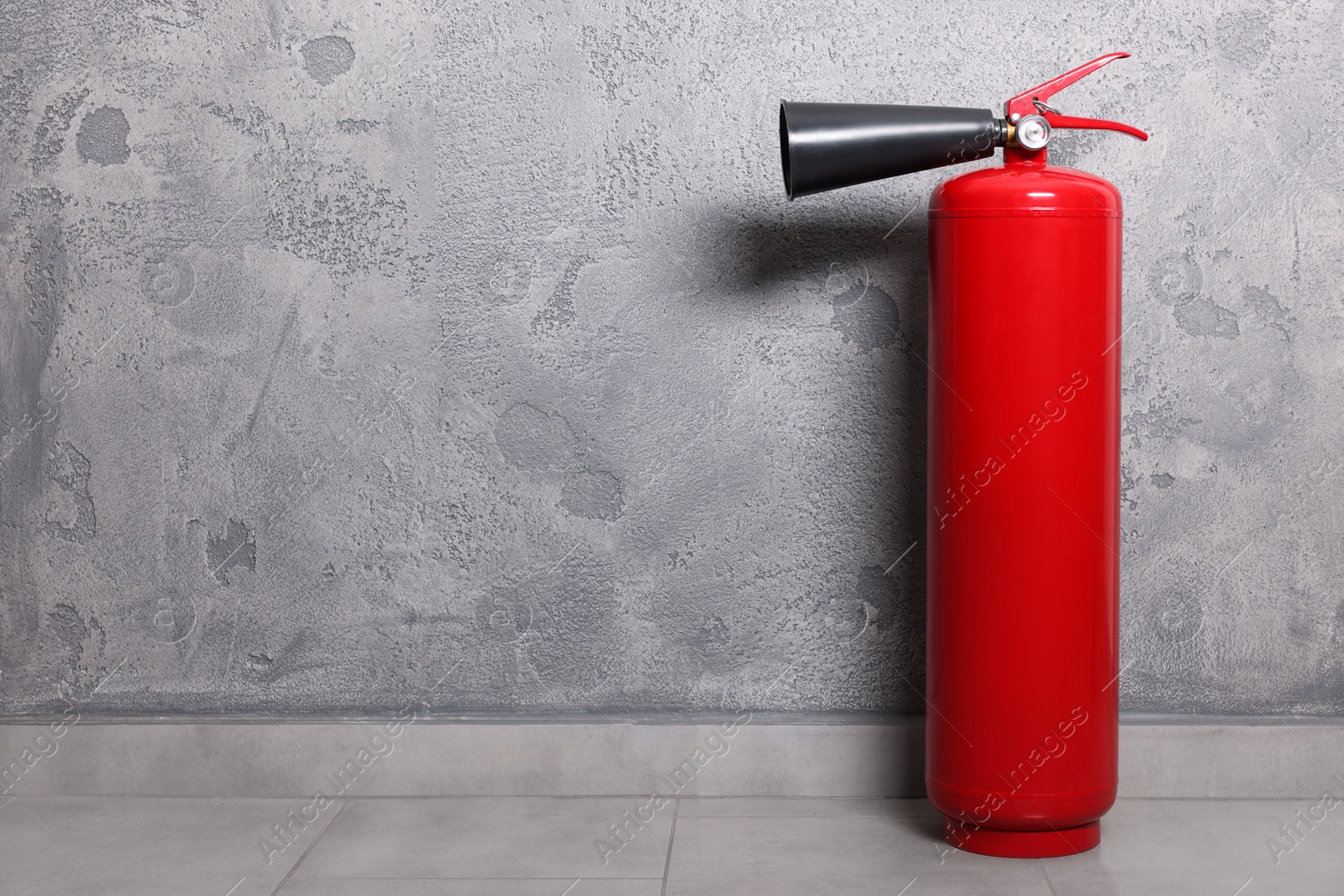 Photo of Red fire extinguisher near grey wall, space for text