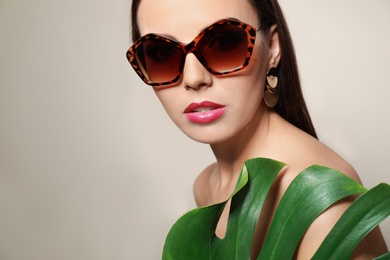 Photo of Beautiful woman in stylish sunglasses with tropical leaf on beige background