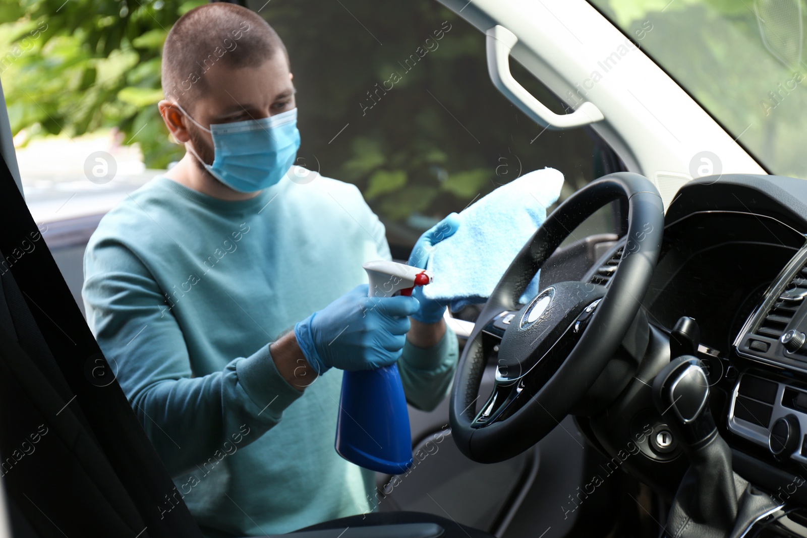 Photo of Man in gloves and mask cleaning car with disinfectant spray and rag. Preventive measure during coronavirus pandemic