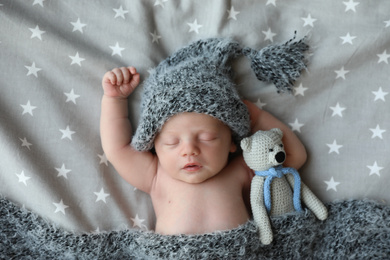 Cute newborn baby in warm hat with toy sleeping on bed, top view