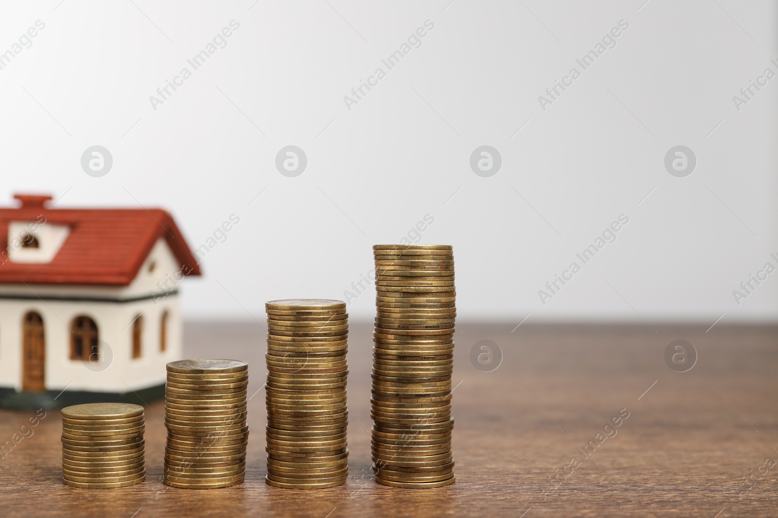 Photo of Mortgage concept. House model and stacks of coins on wooden table against white background, selective focus. Space for text