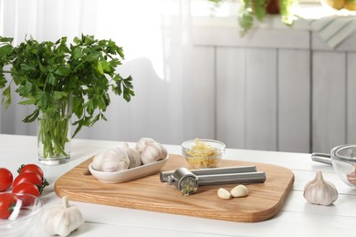 Garlic press and products on wooden table in kitchen
