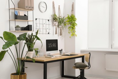 Cozy workplace with computer, modern furniture and houseplants at home