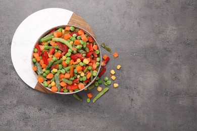 Mix of different frozen vegetables in bowl on grey table, top view. Space for text