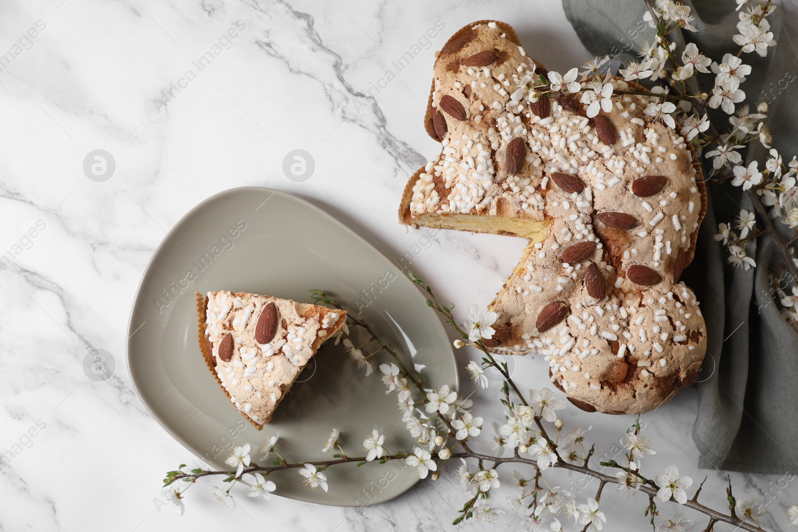 Photo of Delicious Italian Easter dove cake (traditional Colomba di Pasqua) and flowers on white marble table, flat lay. Space for text