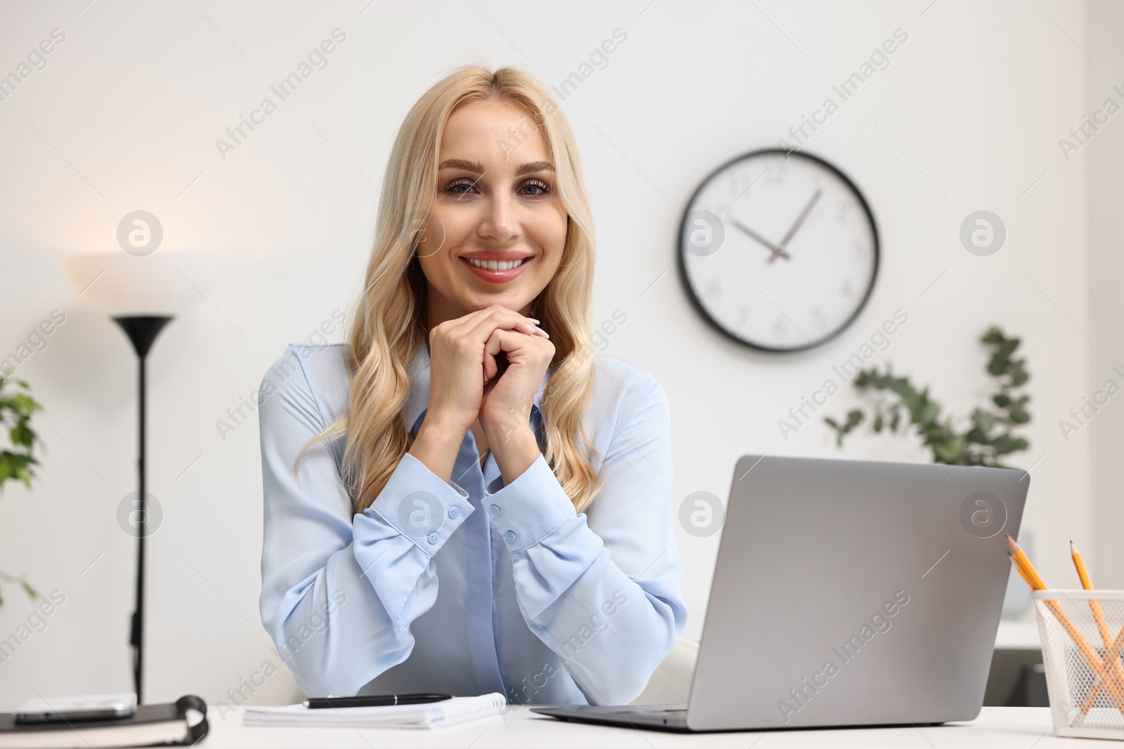 Photo of Happy secretary at table with laptop and stationery in office