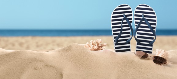 Striped flip flops, coral, sea shell and sunglasses on sandy beach, space for text. Banner design