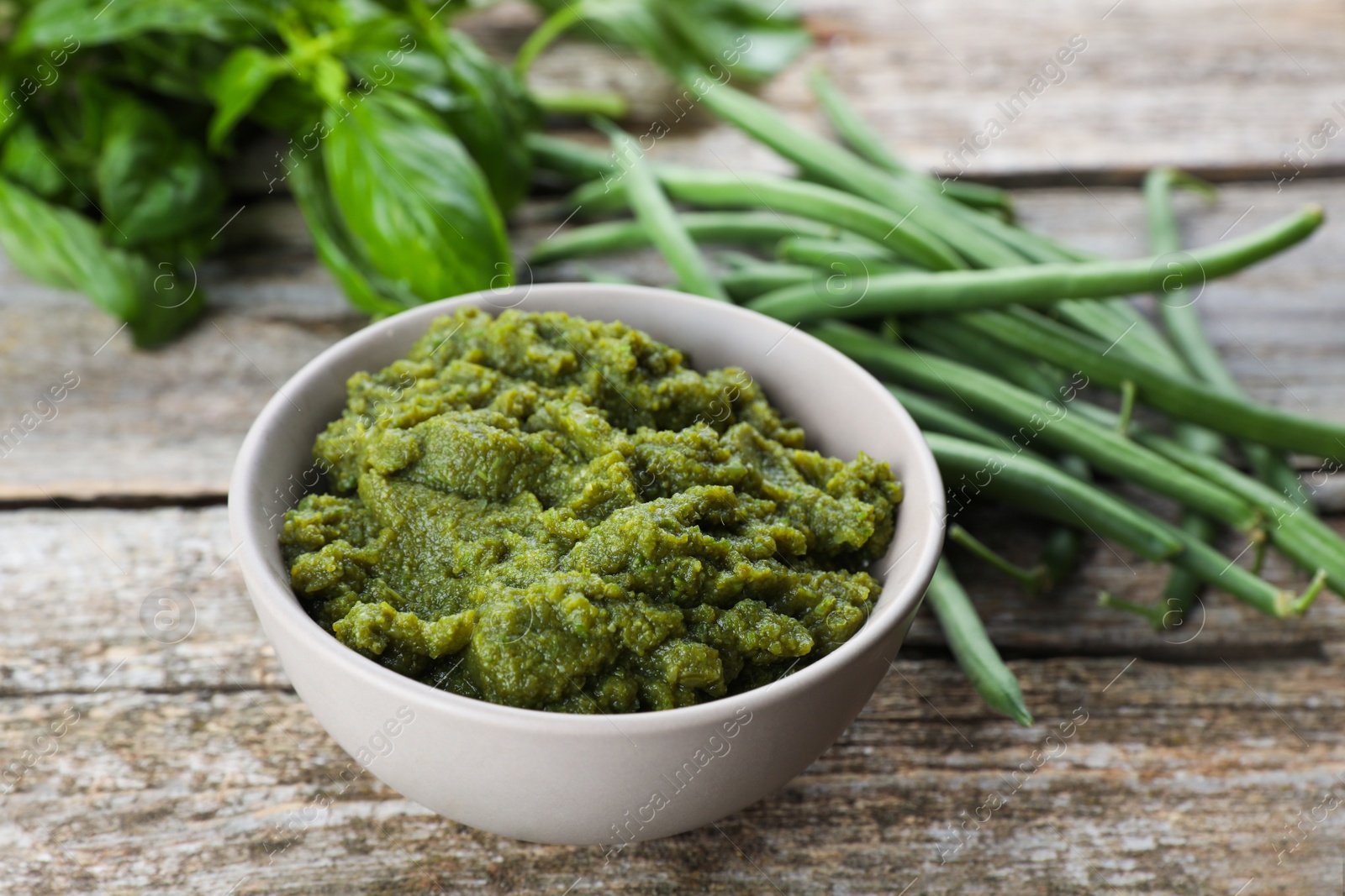 Photo of Bowl with tasty puree, green beans and basil on wooden table, closeup