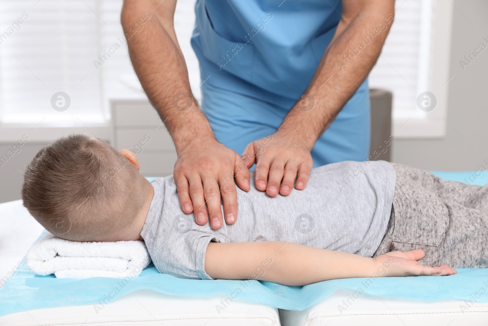 Photo of Orthopedist massaging child's back in clinic, closeup. Scoliosis treatment