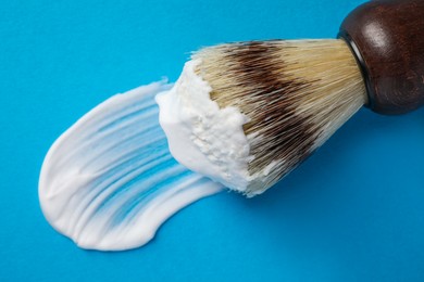 Photo of Brush with shaving foam on blue background, closeup