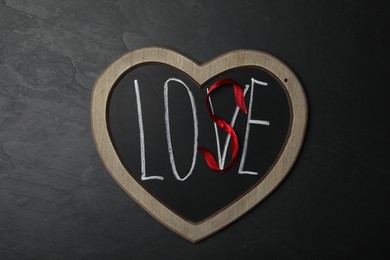 Photo of Heart shaped blackboard with word LOVE and letter S of red ribbon on dark background, top view. Composition symbolizing problems in relationship