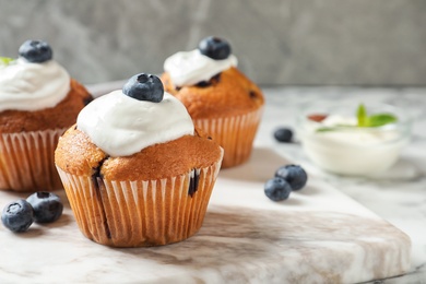 Photo of Marble board with tasty muffins, cream and blueberries on table