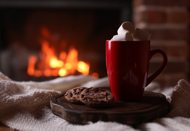 Delicious sweet cocoa with marshmallows, cookies and blurred fireplace on background