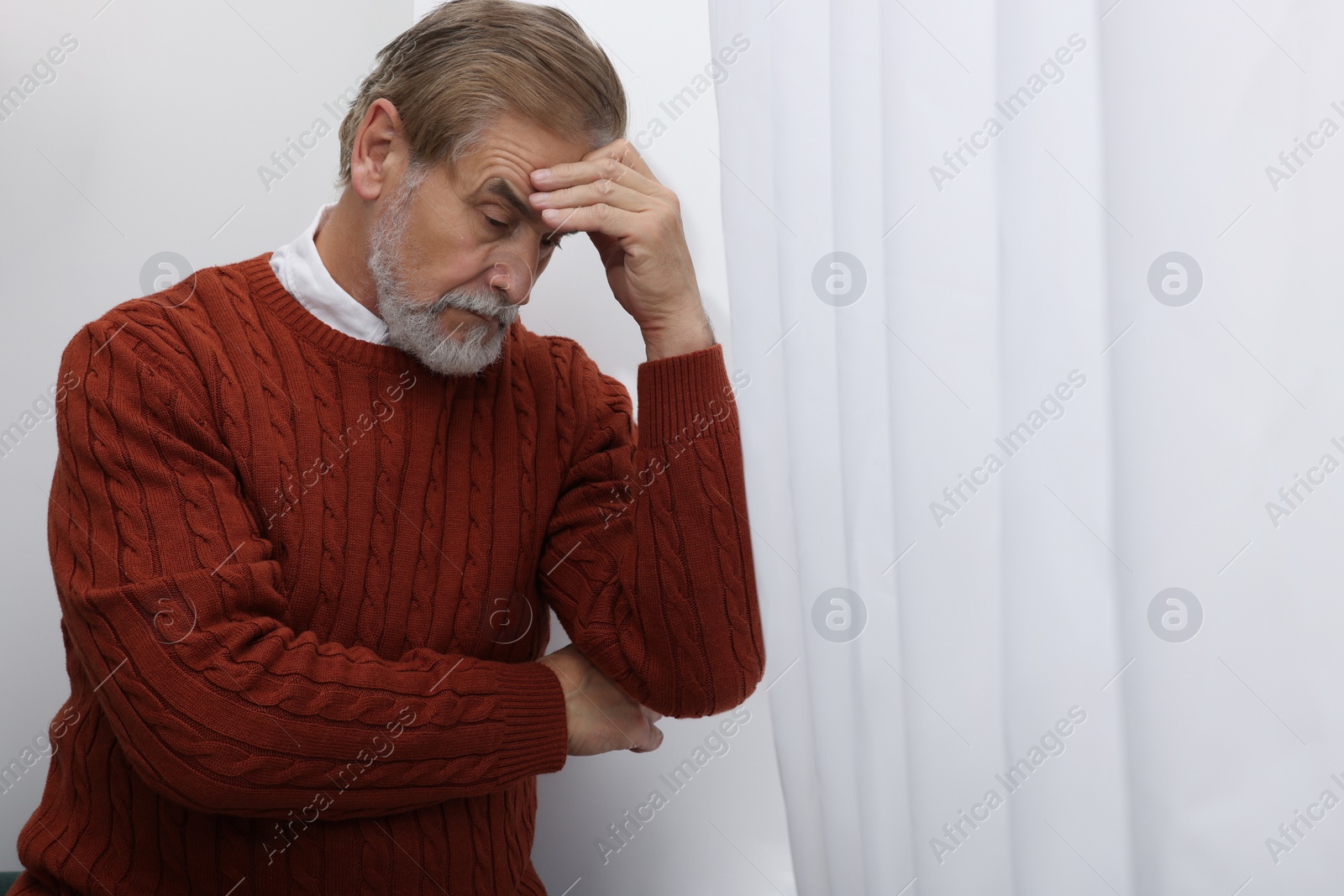 Photo of Upset senior man near window at home. Loneliness concept