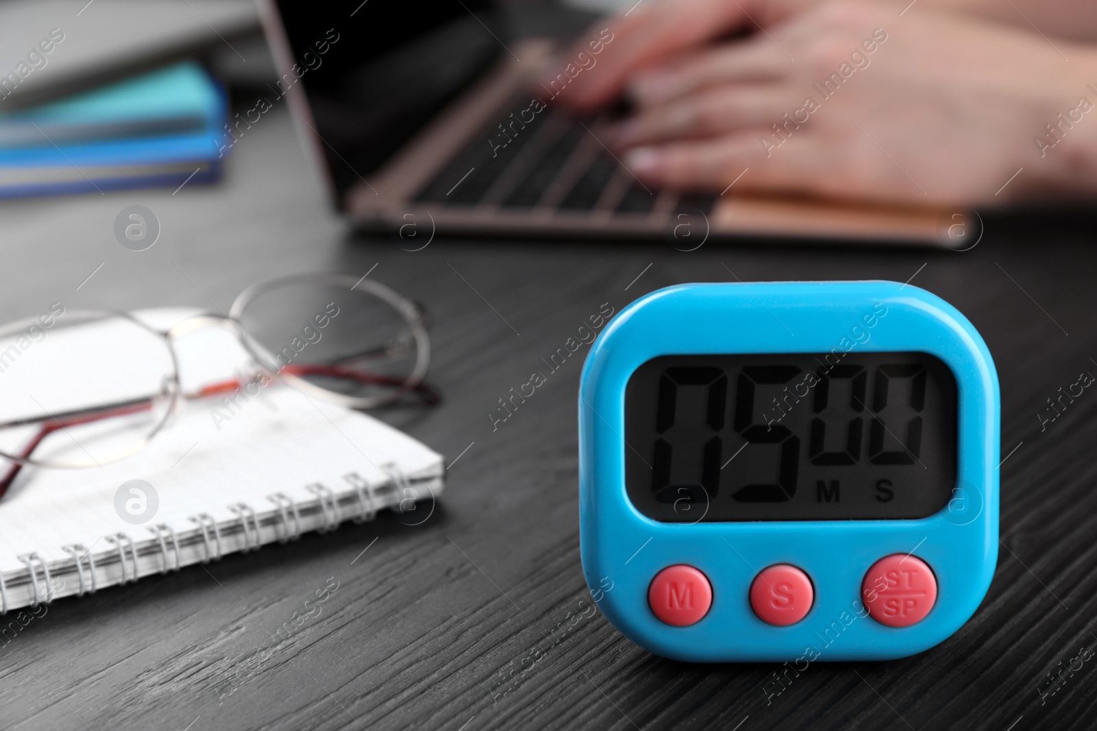 Photo of Woman working on laptop at wooden table, focus on kitchen timer. Space for text