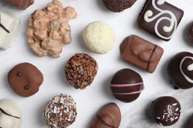 Photo of Different tasty chocolate candies on white marble table, flat lay