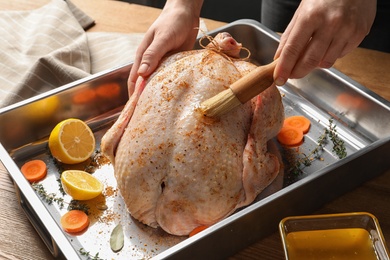 Photo of Woman marinating whole turkey at table, closeup