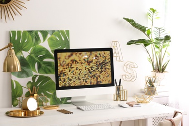 Photo of Modern workplace with computer and golden decor on desk near wall. Stylish interior design