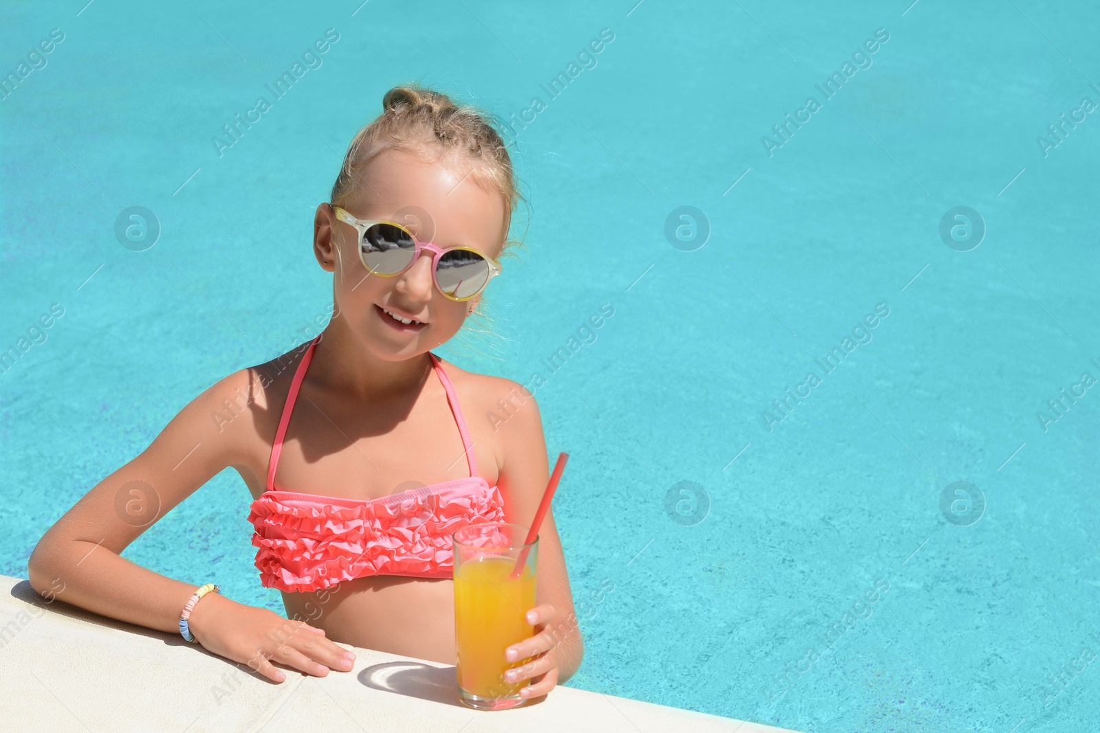 Photo of Cute little girl with glass of juice in swimming pool on sunny day. Space for text