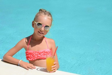 Cute little girl with glass of juice in swimming pool on sunny day. Space for text