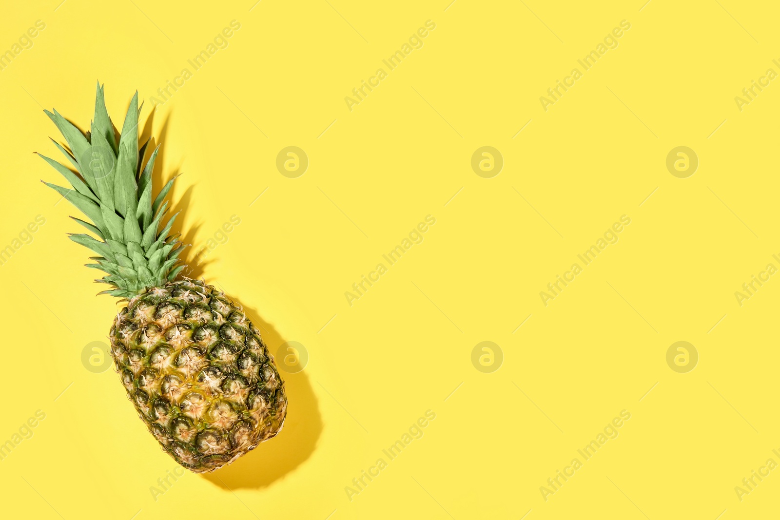 Photo of Whole ripe pineapple on yellow background, top view. Space for text