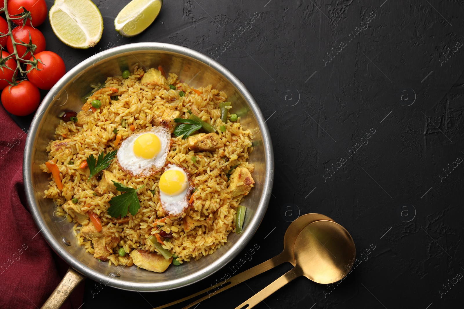 Photo of Tasty rice with meat, eggs and vegetables in frying pan near products on black textured table, flat lay. Space for text