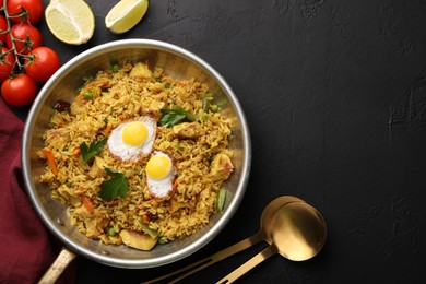 Photo of Tasty rice with meat, eggs and vegetables in frying pan near products on black textured table, flat lay. Space for text