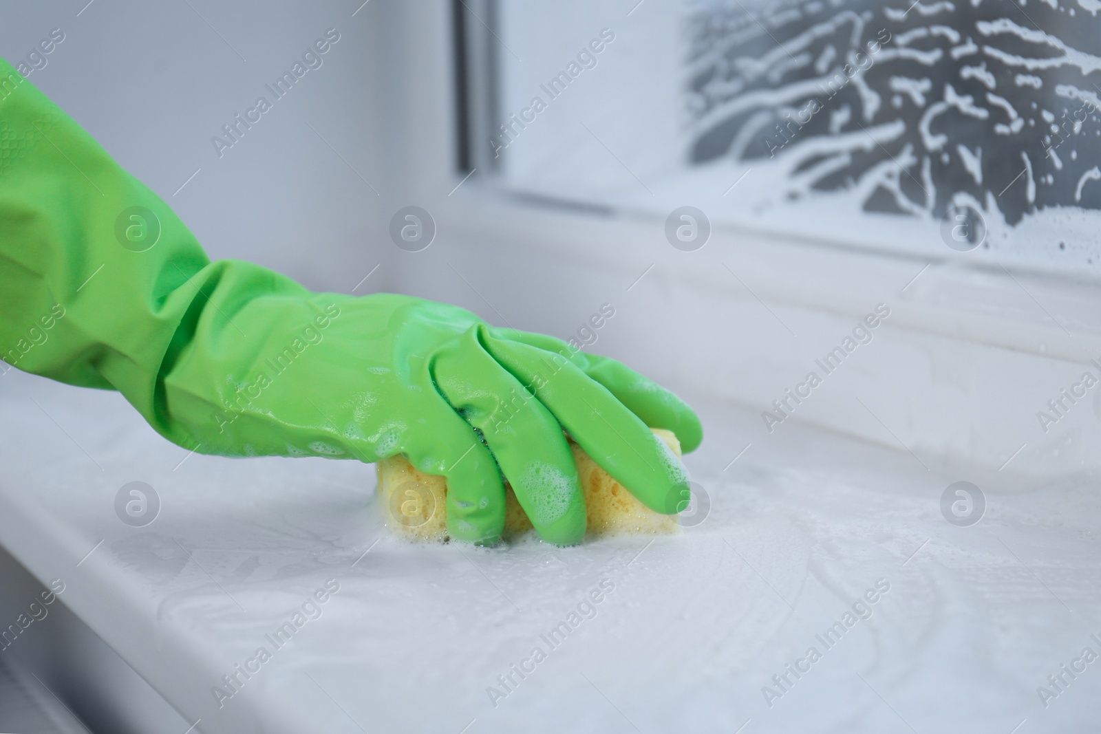 Photo of Woman cleaning window sill with sponge indoors, closeup