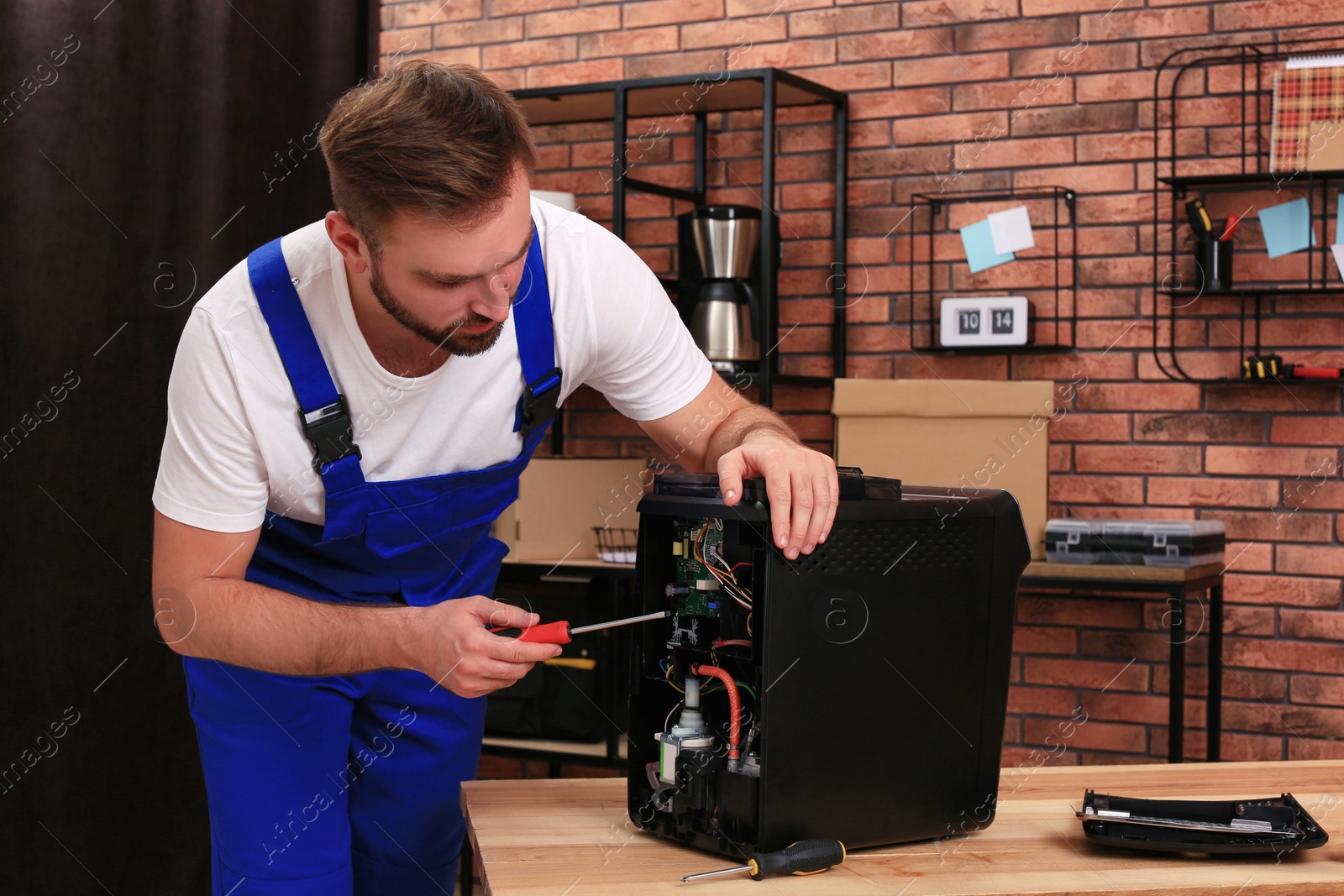 Photo of Repairman with screwdriver fixing coffee machine at table indoors