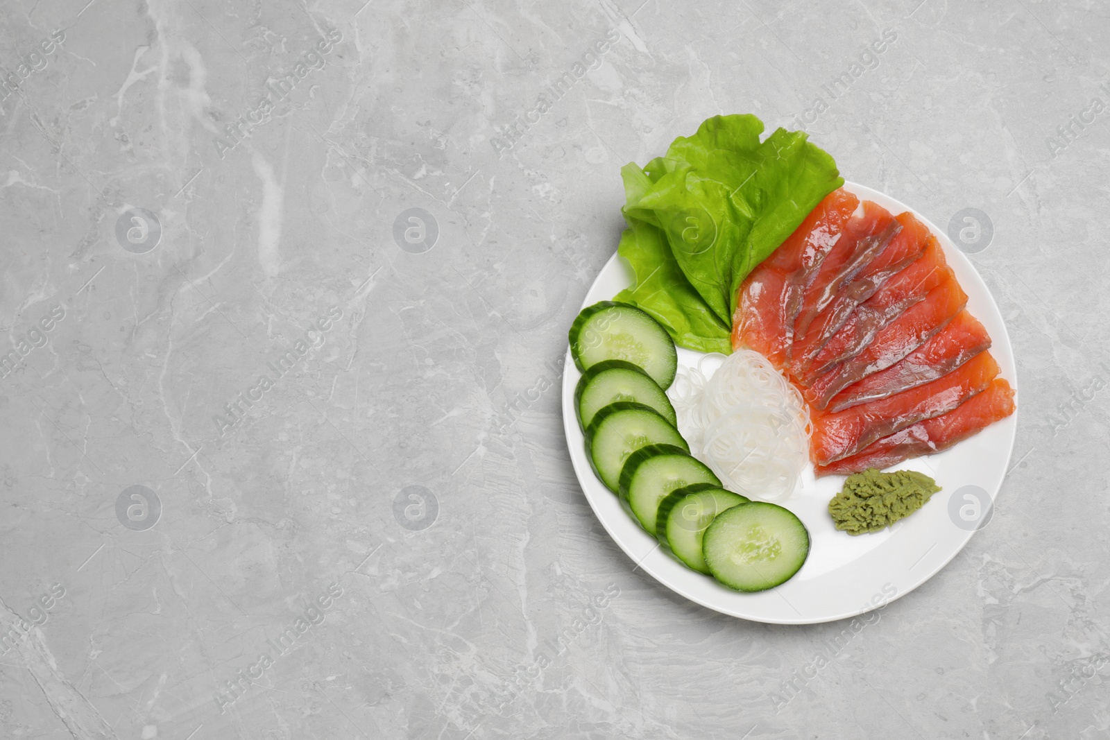 Photo of Sashimi set (salmon slices) with cucumber, greens, vasabi and funchosa on light grey table, top view. Space for text