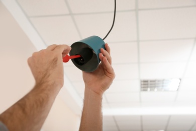 Electrician with screwdriver repairing ceiling lamp indoors, closeup. Space for text