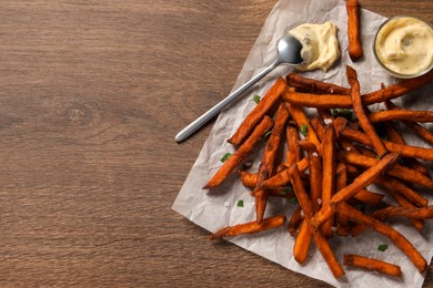 Photo of Delicious sweet potato fries and sauce on wooden table, top view. Space for text