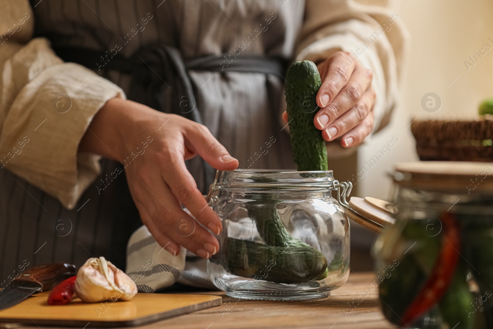 Photo of Woman putting cucumbers into jar at wooden table, closeup. Pickling vegetables