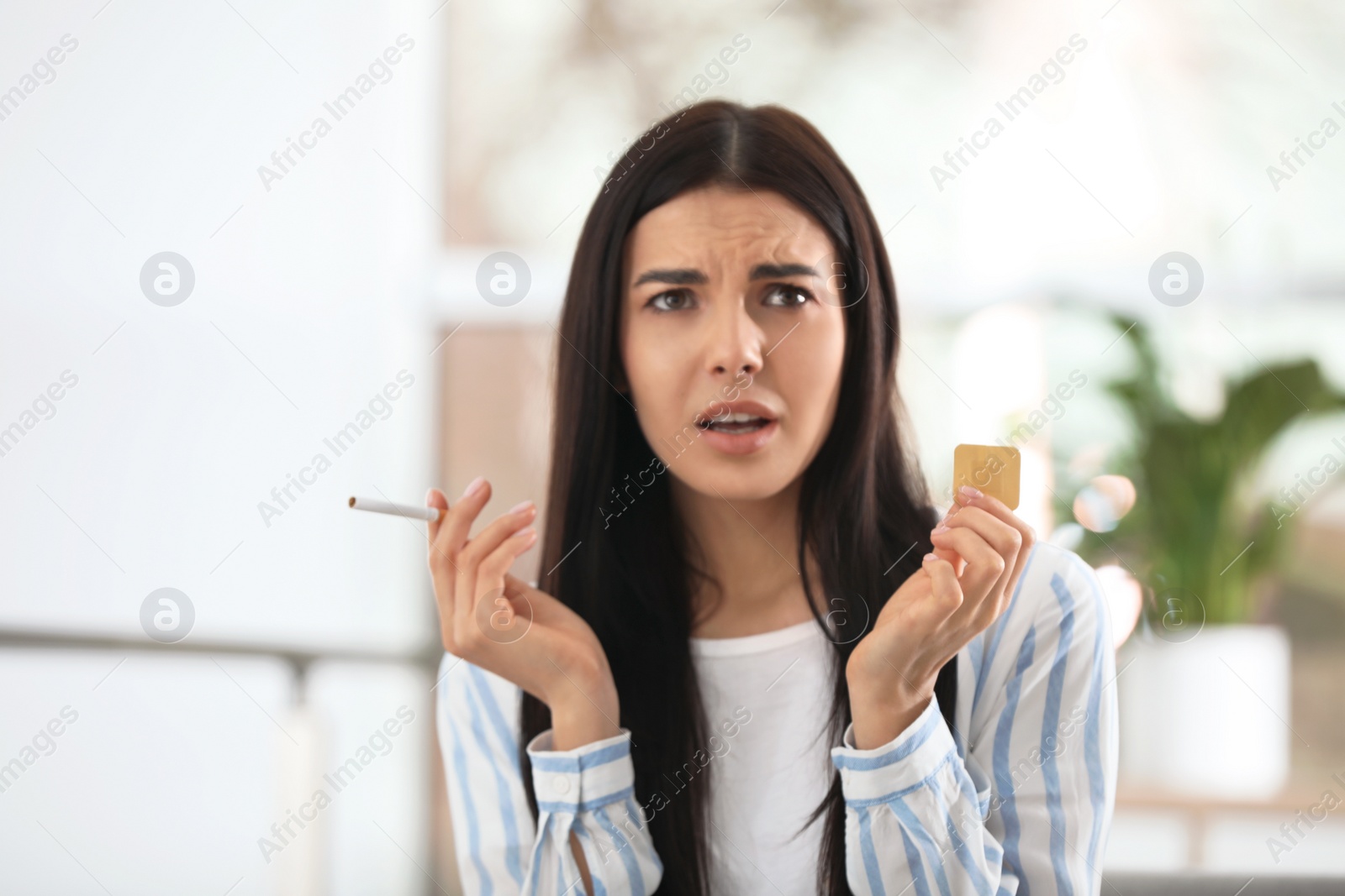 Photo of Emotional young woman with nicotine patch and cigarette at home